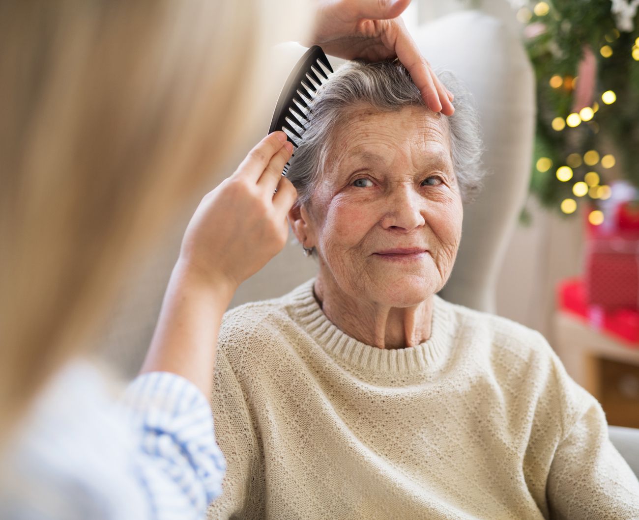 Eine Frau kämmt das Haar einer älteren Dame, die entspannt und zufrieden aussieht.