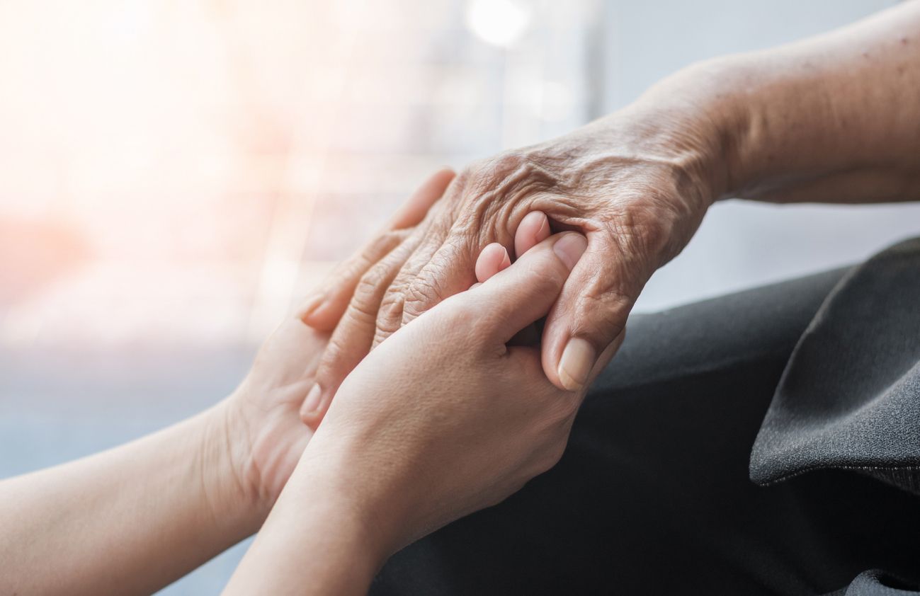 Eine ältere Dame und eine junge Frau halten Händchen, was die starke Bindung und Unterstützung zwischen den Generationen zeigt.