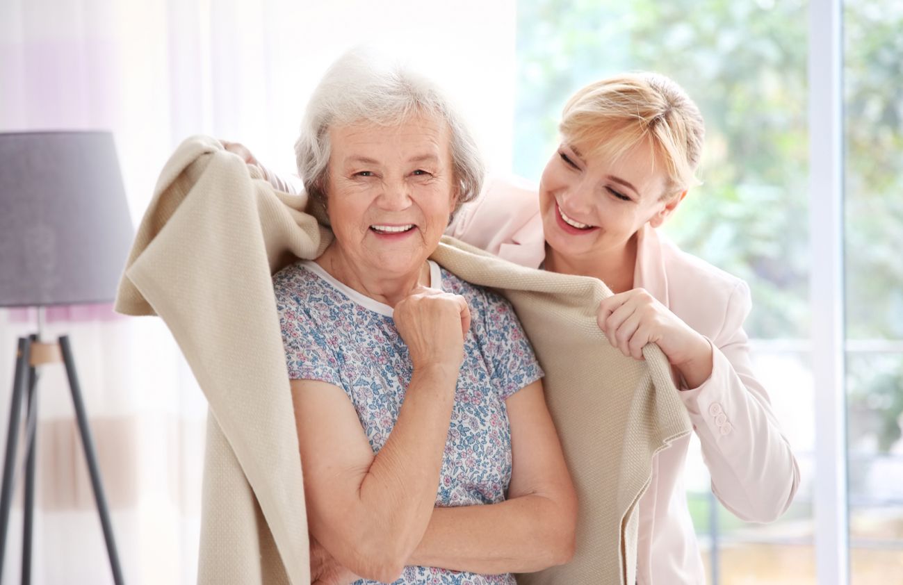 Eine Frau legt einer älteren Dame eine Decke über, um ihr Wärme und Unterstützung in einem fürsorglichen Moment zu geben.