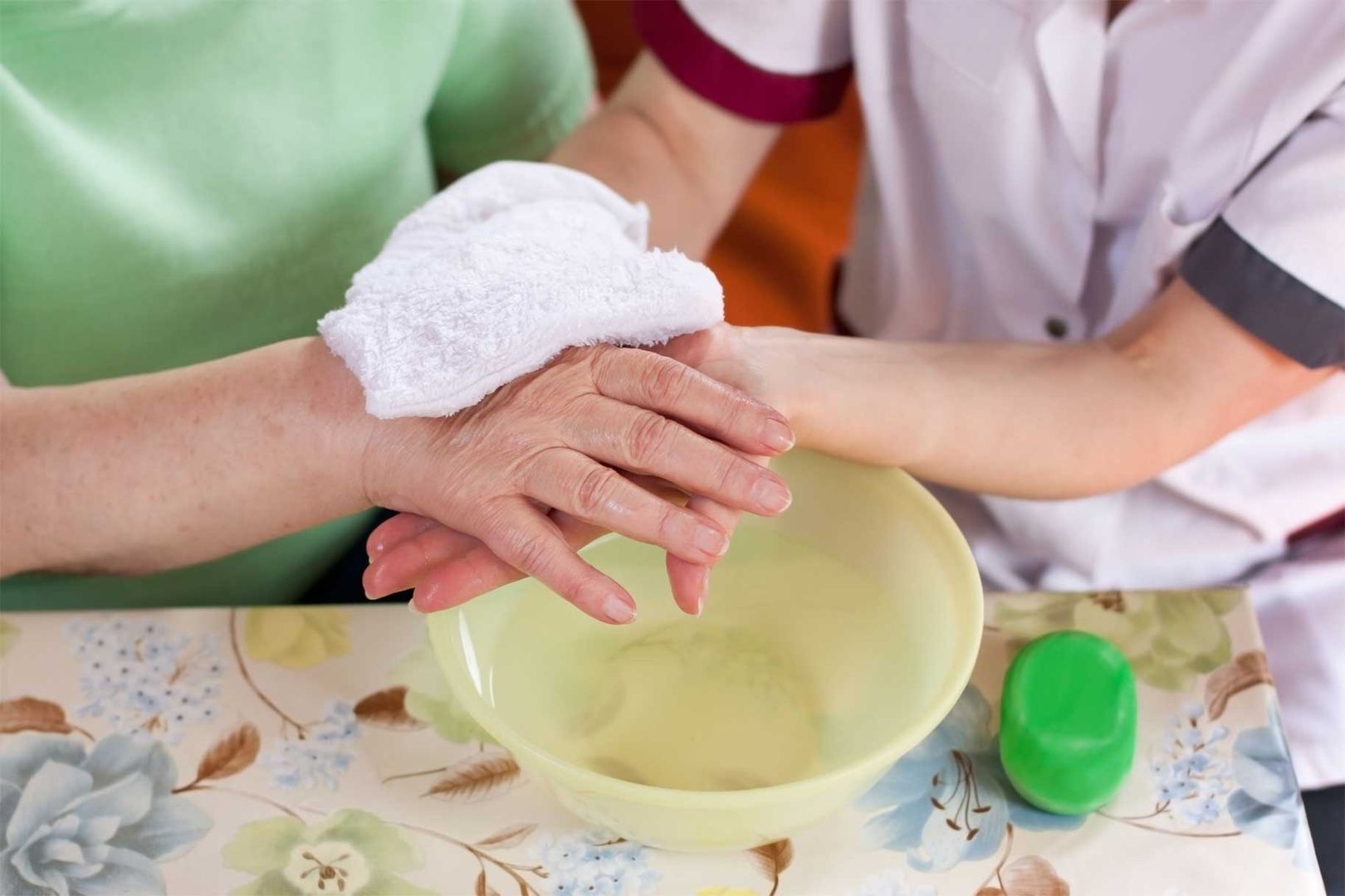 Hand einer älteren Person wird von einer Pflegerin gewaschen
