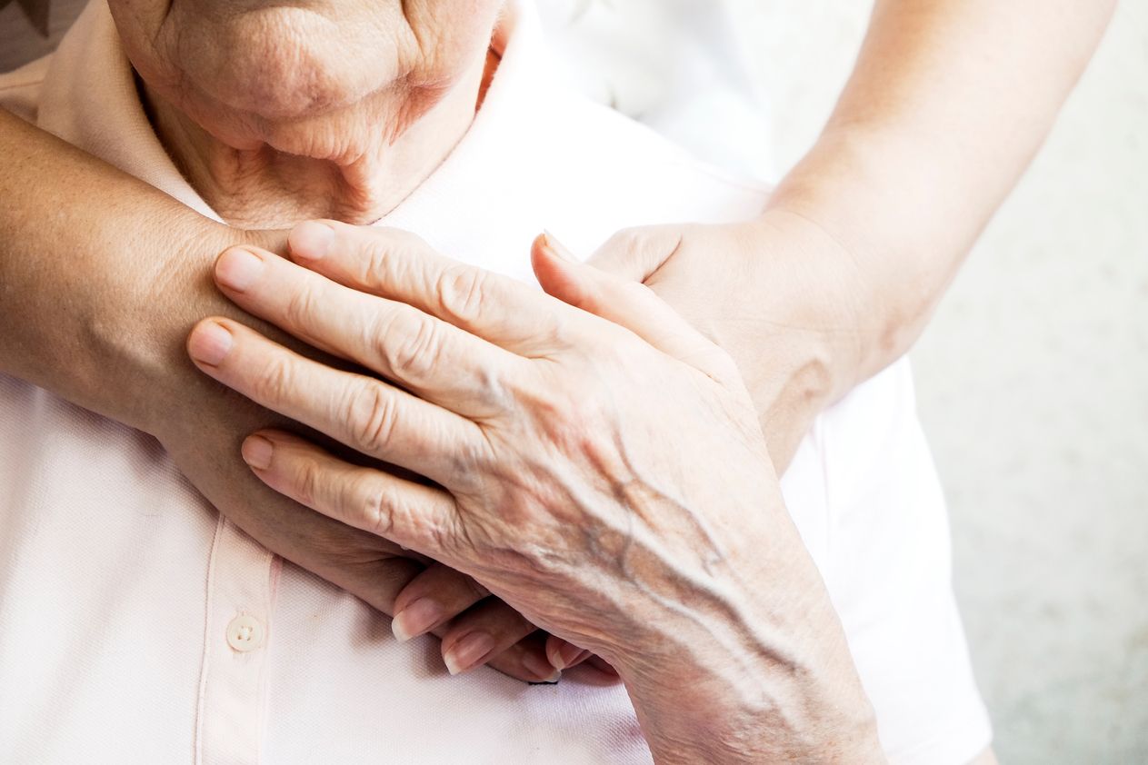 Pflegerin legt ihre Hände auf die Herzseite der Brust einer älteren Person, welche ihrerseits ihre Hand darauf legt
